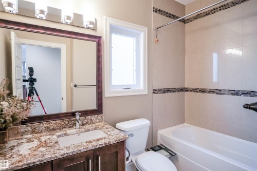 Bathroom featuring a vanity with a granite countertop and an undermount sink, a framed mirror, and a bathtub with tiled walls - 4016 Mactaggart Drive, Edmonton, AB - Indoor Photo Showing Bathroom