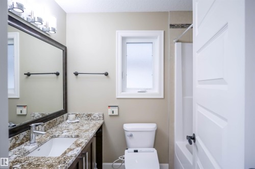 Bathroom featuring a vanity with granite countertop and undermount sink, a large mirror, and a frosted window providing natural light - 4016 Mactaggart Drive, Edmonton, AB - Indoor Photo Showing Bathroom