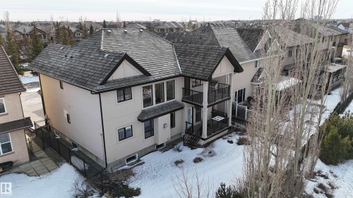 The property features a multi-level design with a prominent shingled roof, two balconies with glass railings, and an exterior of light-colored stucco - 4016 Mactaggart Drive, Edmonton, AB - Outdoor