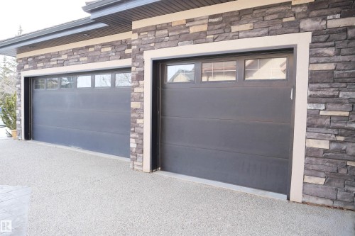 Exterior featuring two garage doors with windows, stone facade, and a light-colored paved driveway - 4016 Mactaggart Drive, Edmonton, AB - Outdoor