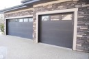 Exterior featuring two garage doors with windows, stone facade, and a light-colored paved driveway - 4016 Mactaggart Drive, Edmonton, AB  - Outdoor 