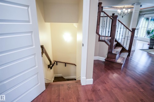The property features hardwood flooring throughout this area, a staircase with dark wood railings and wrought iron spindles, and a separate staircase leading to a lower level - 4016 Mactaggart Drive, Edmonton, AB - Indoor Photo Showing Other Room