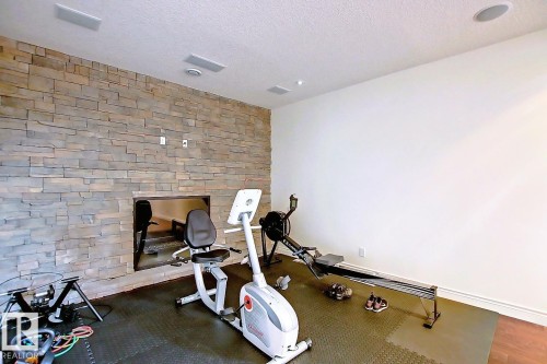 This versatile room features a stone accent wall with an integrated fireplace, recessed lighting, and built-in speakers - 4016 Mactaggart Drive, Edmonton, AB - Indoor Photo Showing Gym Room