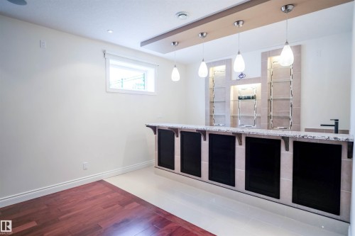 This space features a bar area with a light-colored countertop, dark cabinetry, and a black faucet - 4016 Mactaggart Drive, Edmonton, AB - Indoor Photo Showing Other Room