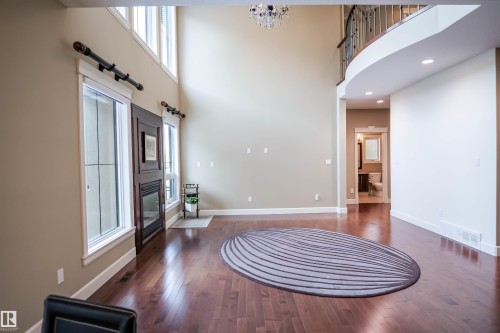This living area features rich hardwood flooring, a fireplace, and tall windows that provide abundant natural light - 4016 Mactaggart Drive, Edmonton, AB - Indoor Photo Showing Other Room