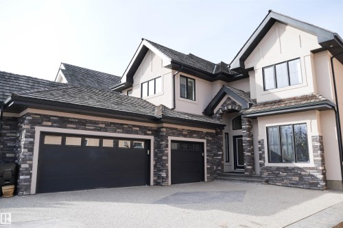 The property features a stone and stucco exterior, dark shingled roof, and a two-car garage with dark doors and frosted windows - 4016 Mactaggart Drive, Edmonton, AB - Outdoor