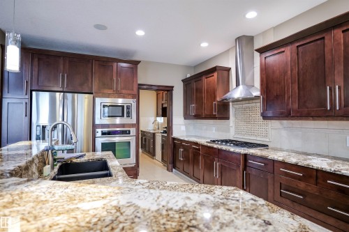 The kitchen features rich wood cabinetry, granite countertops, stainless steel appliances, and an integrated range hood - 4016 Mactaggart Drive, Edmonton, AB - Indoor Photo Showing Kitchen With Double Sink With Upgraded Kitchen
