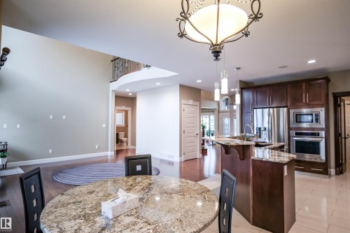 Spacious kitchen and dining area featuring dark wood cabinetry, stainless steel appliances, and granite countertops - 4016 Mactaggart Drive, Edmonton, AB - Indoor Photo Showing Kitchen With Upgraded Kitchen