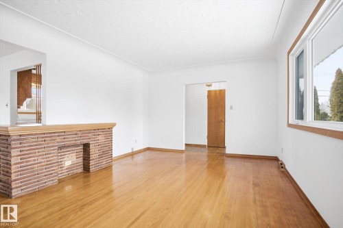 This interior space features light hardwood floors, white walls, and a brick fireplace - 6503 106A Avenue, Edmonton, AB - Indoor Photo Showing Other Room With Fireplace