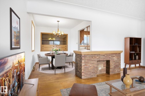 The main living area features hardwood floors, a brick fireplace, and a dining area with a chandelier - 6503 106A Avenue, Edmonton, AB - Indoor With Fireplace