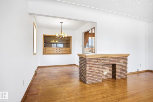 Spacious living area featuring hardwood flooring, a brick fireplace, and a built-in wooden display cabinet - 6503 106A Avenue, Edmonton, AB - Indoor With Fireplace