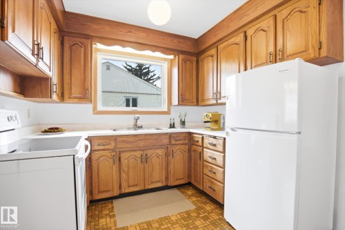 The kitchen features wooden cabinetry, white countertops, a white refrigerator, and a window above the sink - 6503 106A Avenue, Edmonton, AB - Indoor Photo Showing Kitchen With Double Sink