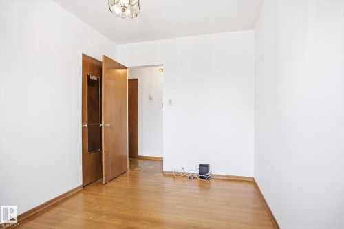 This space features bright white walls and hardwood flooring, complemented by a decorative ceiling light fixture - 6503 106A Avenue, Edmonton, AB - Indoor Photo Showing Other Room