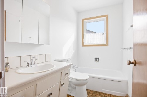 This bathroom features a vanity with an integrated sink and base cabinets, a mirrored medicine cabinet, and a bathtub with an overhead window - 6503 106A Avenue, Edmonton, AB - Indoor Photo Showing Bathroom