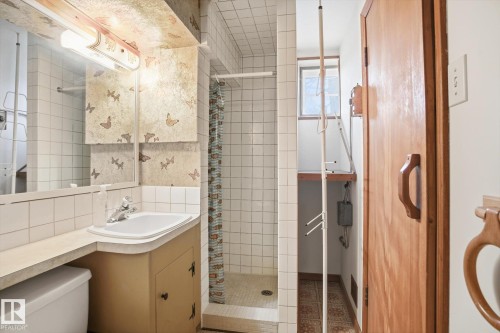 This bathroom features a vanity with a sink and storage, a tiled shower, and a window providing natural light - 6503 106A Avenue, Edmonton, AB - Indoor Photo Showing Bathroom