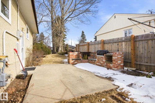 The property features a concrete patio area, a wood fence, and a brick-built outdoor cooking structure - 6503 106A Avenue, Edmonton, AB - Outdoor