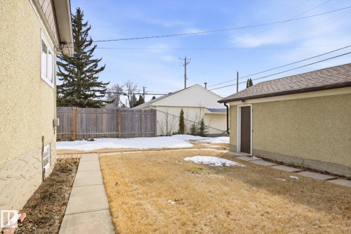 The property features a spacious yard with a concrete pathway and a detached garage with a side door access - 6503 106A Avenue, Edmonton, AB - Outdoor