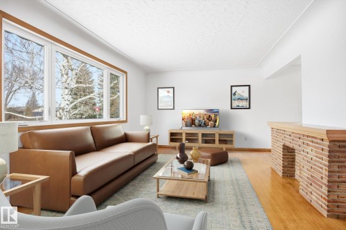 The living room features large windows with wood trim, hardwood floors, and a decorative brick structure - 6503 106A Avenue, Edmonton, AB - Indoor Photo Showing Living Room