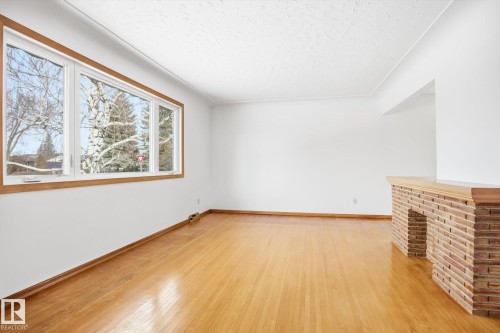 The property features hardwood floors, a large window with wooden trim, and a brick fireplace with a wooden mantel - 6503 106A Avenue, Edmonton, AB - Indoor Photo Showing Other Room