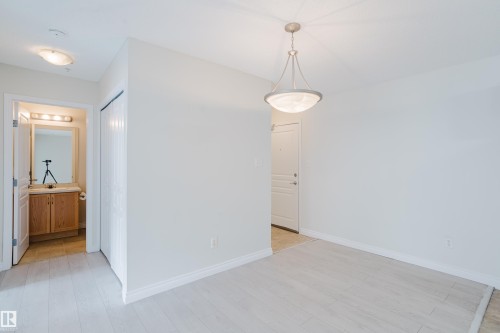 Entryway featuring light-toned flooring, a modern chandelier, and access to a bathroom with a wooden vanity and mirror - 113 309 Clareview Station Drive, Edmonton, AB - Indoor Photo Showing Other Room