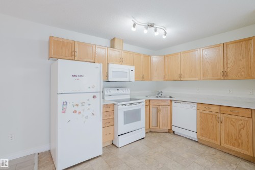 The kitchen features light wood cabinetry, white appliances, and track lighting - 113 309 Clareview Station Drive, Edmonton, AB - Indoor Photo Showing Kitchen