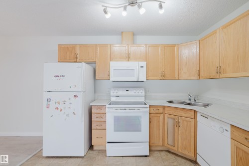 The kitchen features light wood cabinetry, white appliances, and a dual stainless steel sink - 113 309 Clareview Station Drive, Edmonton, AB - Indoor Photo Showing Kitchen With Double Sink