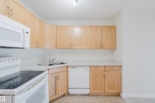 The kitchen features light wood cabinetry, white countertops, and white appliances including a microwave, stove, and dishwasher - 113 309 Clareview Station Drive, Edmonton, AB - Indoor Photo Showing Kitchen With Double Sink