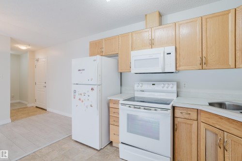 The kitchen features light wood cabinetry, white appliances, and a double basin sink - 113 309 Clareview Station Drive, Edmonton, AB - Indoor Photo Showing Kitchen