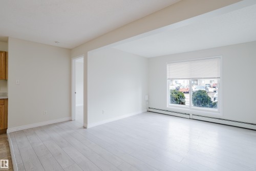 This bright living area features light-toned flooring and a large window, providing natural illumination - 113 309 Clareview Station Drive, Edmonton, AB - Indoor