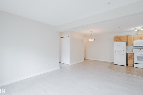 Open concept living area featuring light-toned flooring, white walls, and a kitchen area with wooden cabinetry and white appliances - 113 309 Clareview Station Drive, Edmonton, AB - Indoor Photo Showing Kitchen