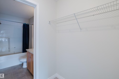 This space features a wire shelf and offers a view into a bathroom with a white tub, a toilet, and a light wood vanity - 113 309 Clareview Station Drive, Edmonton, AB - Indoor With Storage