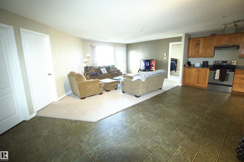 Open concept living area featuring a kitchen with wood cabinetry and stainless steel appliances, and a living room with carpet flooring - 1204 330 Clareview Station Drive, Edmonton, AB - Indoor