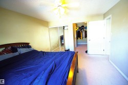 This bedroom features light-colored walls, carpeted flooring, and a ceiling fan with illumination - 