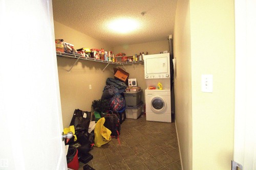 This utility area features a tiled floor, a stacked washer and dryer, and wire shelving for storage - 1204 330 Clareview Station Drive, Edmonton, AB - Indoor Photo Showing Laundry Room