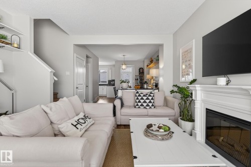 The living area features light-colored walls, a prominent fireplace with a mantel, and an entryway to another part of the home - 9084 Rosenthal Link, Edmonton, AB - Indoor Photo Showing Living Room With Fireplace