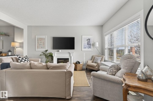 Living room featuring dark wood flooring, a fireplace with a white mantel, and a large window with blinds - 9084 Rosenthal Link, Edmonton, AB - Indoor Photo Showing Living Room With Fireplace