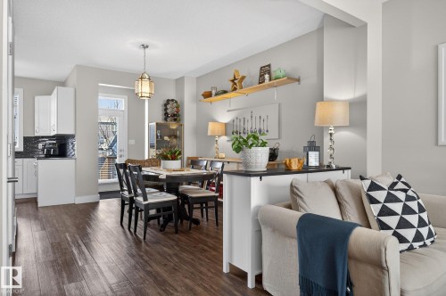 Open concept living space featuring hardwood floors, a dining area with a modern chandelier, and a kitchen with white cabinetry and dark backsplash - 9084 Rosenthal Link, Edmonton, AB - Indoor Photo Showing Dining Room