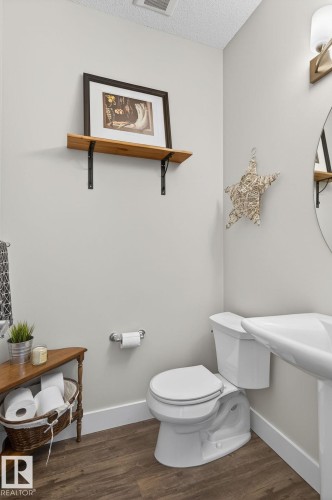 This bathroom features wood-look flooring, a white pedestal sink, and a white toilet - 9084 Rosenthal Link, Edmonton, AB - Indoor Photo Showing Bathroom