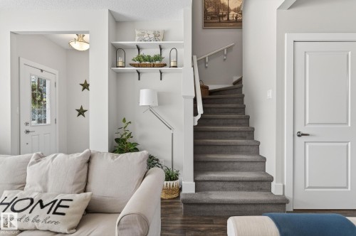 Inviting living space featuring dark wood-look flooring, a white paneled entry door with frosted glass, and a carpeted staircase with white railings - 9084 Rosenthal Link, Edmonton, AB - Indoor Photo Showing Other Room