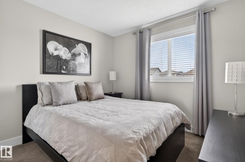 This bedroom features light-colored walls, carpeted flooring, and a window with blinds and drapes - 9084 Rosenthal Link, Edmonton, AB - Indoor Photo Showing Bedroom