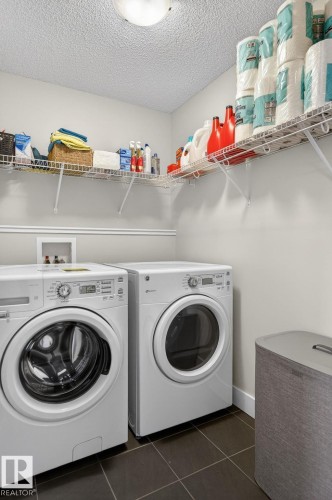 Dedicated laundry area featuring a front-loading washing machine and dryer, overhead wire shelving, and tiled flooring - 9084 Rosenthal Link, Edmonton, AB - Indoor Photo Showing Laundry Room