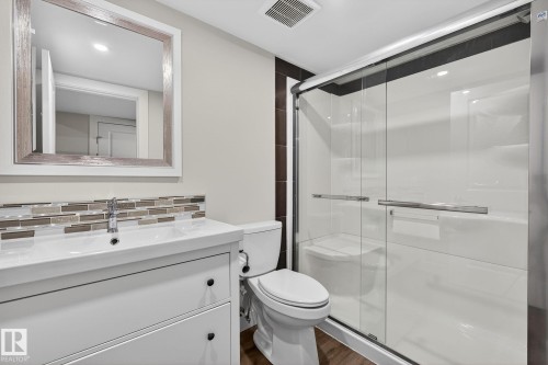 The bathroom features a modern vanity with a white countertop and a contemporary sink, complemented by a mosaic tile backsplash - 9084 Rosenthal Link, Edmonton, AB - Indoor Photo Showing Bathroom