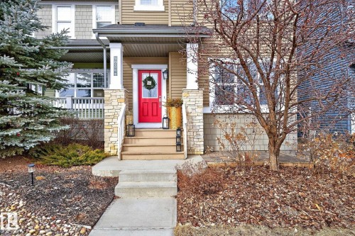 The property features a red front door with a wreath, a covered porch with white railings, and stone-accented pillars - 9084 Rosenthal Link, Edmonton, AB - Outdoor With Facade