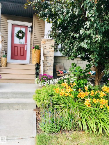 The property features an inviting entrance with a red front door, exterior lighting, and a stone-clad pillar - 9084 Rosenthal Link, Edmonton, AB - Outdoor