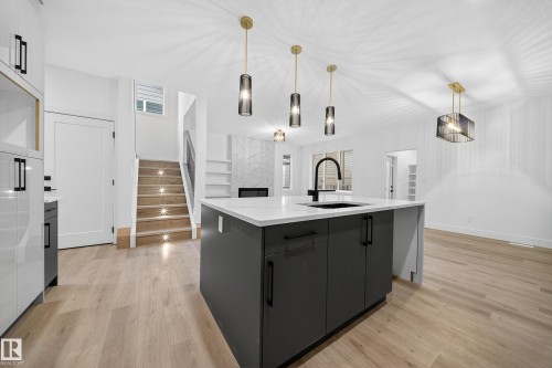 The property features an open-concept living space with light wood flooring, a kitchen island with a dark gray finish and a white countertop, and contemporary pendant lighting fixtures - 6117 Crawford Drive, Edmonton, AB 