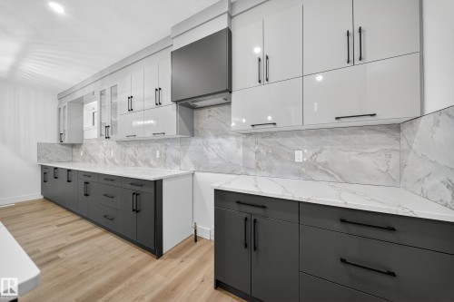 The modern kitchen features light wood flooring, white and gray cabinetry, and a white countertop and backsplash with gray veining - 6117 Crawford Drive, Edmonton, AB 