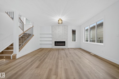 Spacious living area featuring light-colored flooring, a modern fireplace with a tiled surround, built-in shelving, and large windows providing natural light - 6117 Crawford Drive, Edmonton, AB 