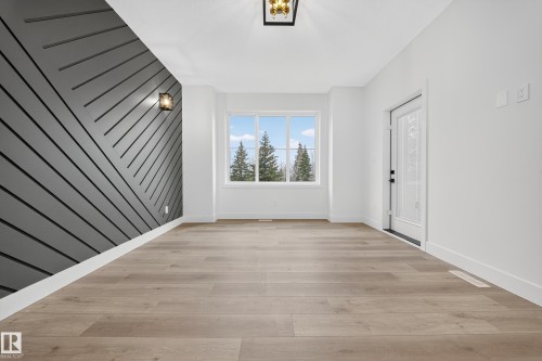 This property features wide plank flooring, a large window with an outdoor view, and a distinctive accent wall with a wall-mounted light fixture - 6117 Crawford Drive, Edmonton, AB 