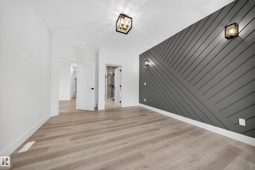 Spacious room featuring light-toned flooring, a distinctive dark accent wall with a geometric pattern, and contemporary ceiling and wall light fixtures - 6117 Crawford Drive, Edmonton, AB 