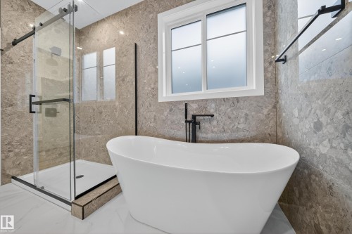 Bathroom featuring a freestanding white bathtub, a glass-enclosed shower, and walls adorned with patterned tiles - 6117 Crawford Drive, Edmonton, AB 